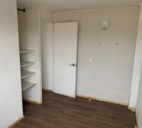 Dormitorio en segundo piso con piso flotante en tono madera, muros claros que aportan luminosidad y un closet abierto con estanterías que optimiza el almacenamiento.