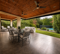 Terraza techada con comedor exterior, zona de descanso, jardín y piscina al fondo.