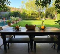 Terraza techada con mesa exterior y vista al jardín y la piscina.