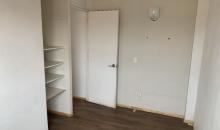 Dormitorio en segundo piso con piso flotante en tono madera, muros claros que aportan luminosidad y un closet abierto con estanterías que optimiza el almacenamiento.