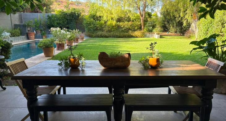 Terraza techada con mesa exterior y vista al jardín y la piscina.