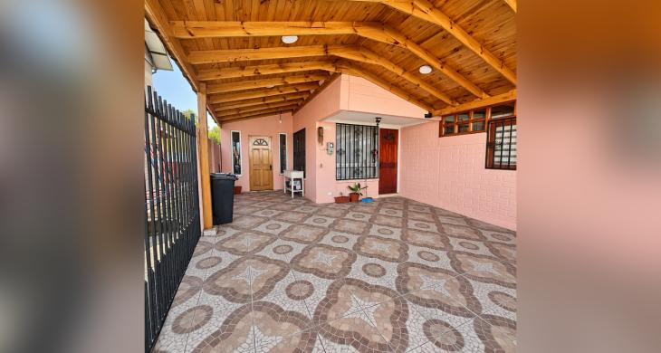 Acceso techado de la casa, con piso de baldosas y estructura de madera.