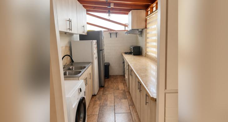 Cocina alargada con muebles a ambos lados, lavaplatos, encimera y techo de madera.